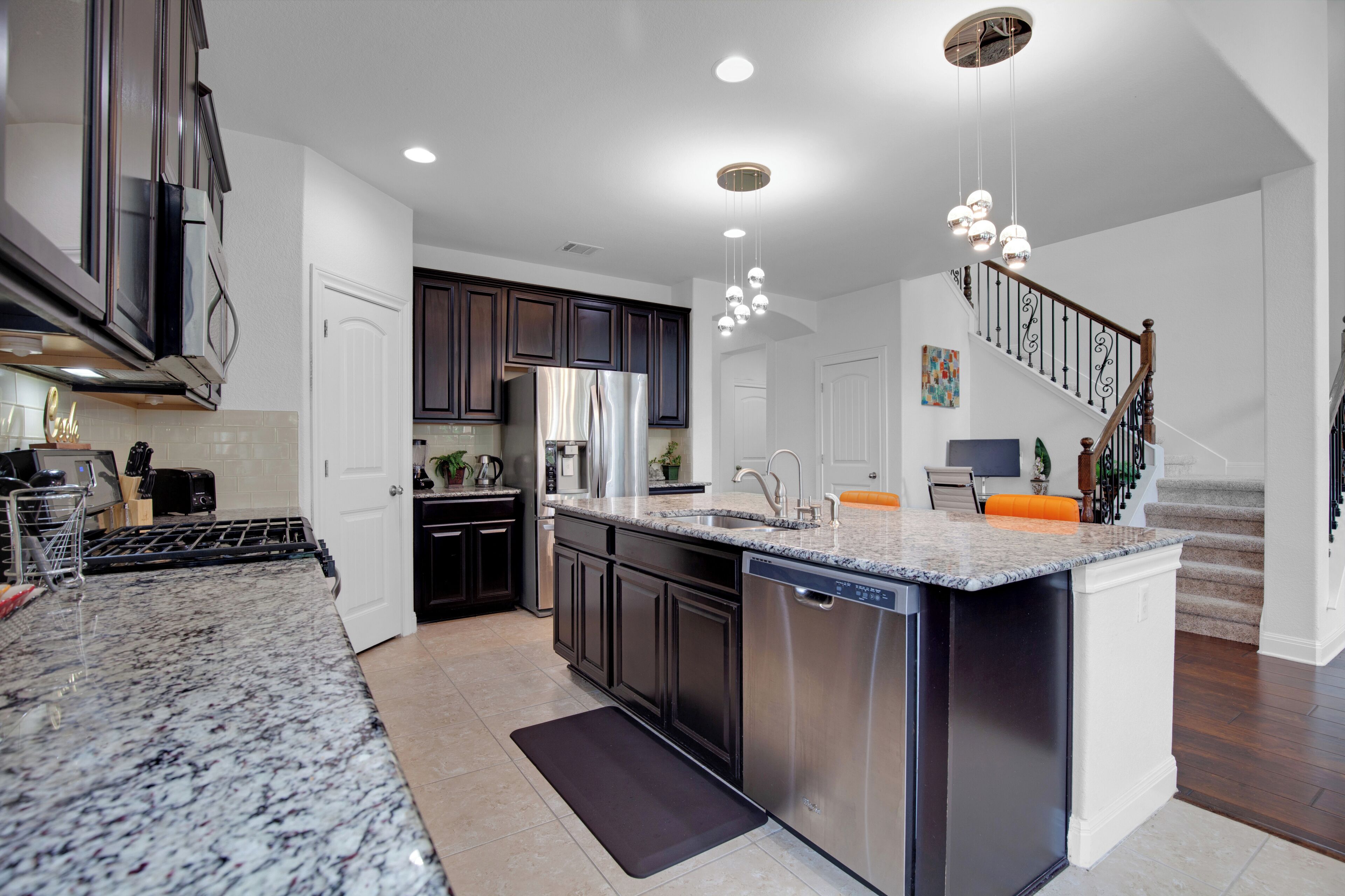 A modern kitchen with dark cabinets, a stainless steel refrigerator, and a granite countertop.