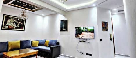 A modern living room with a sofa, coffee table, TV mounted on the wall, and decorative ceiling patterns.