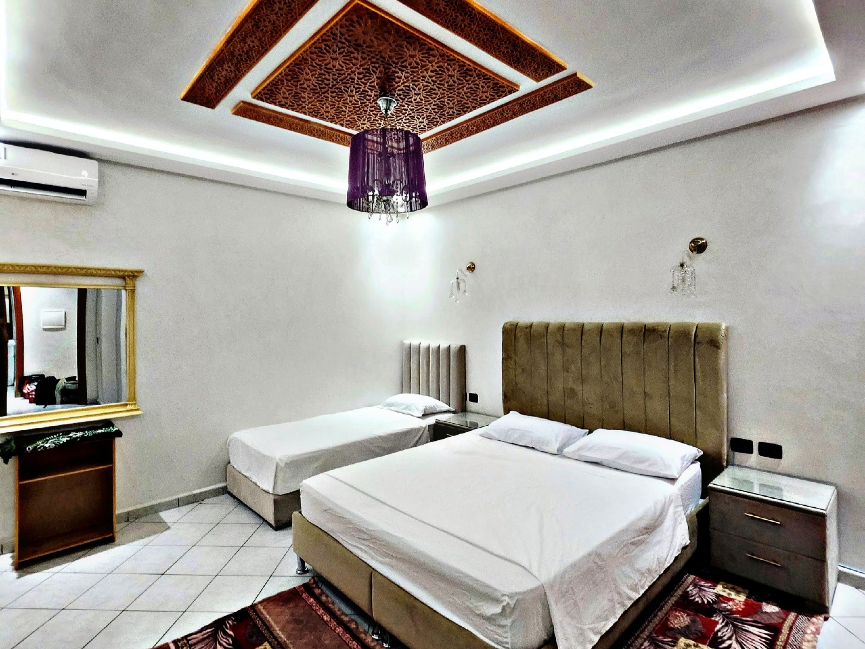 Ein Hotelzimmer mit zwei Betten, einem großen Spiegel, einer Decke mit aufwendigen Mustern und einem modernen Kronleuchter.