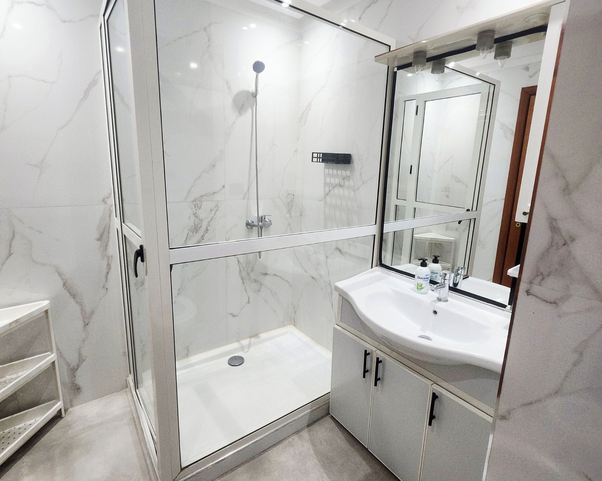 A modern bathroom with a glass-enclosed shower, a white sink, and a large mirror.