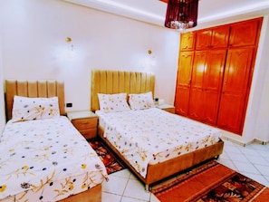 A bedroom with two beds, a wardrobe, and a nightstand.