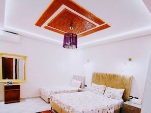 A bedroom with two beds, a mirror, a nightstand, and a ceiling with intricate patterns.