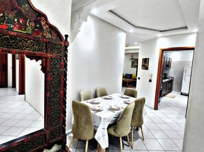 Un coin repas avec une table dressée pour quatre personnes, entourée de chaises, et un paravent décoratif aux motifs complexes.