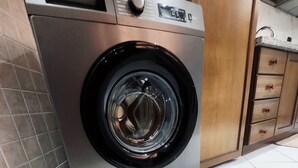 A front-loading washing machine with a control panel, located in a kitchen area with wooden cabinets and a tiled floor. - Modern apartment Guéliz center - spacious - Parking (Marrakech)