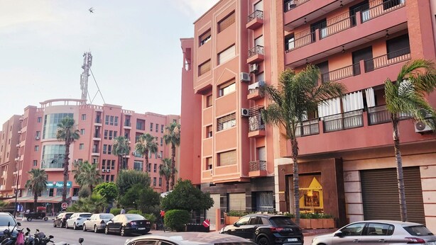 A multi-story building with balconies, parked cars, and palm trees. - Modern apartment Guéliz center - spacious - Parking (Marrakech)