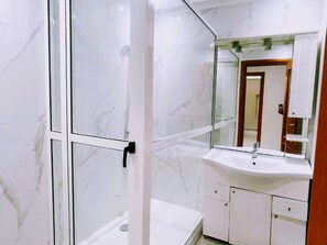A bathroom with a glass shower enclosure, a white sink, and a mirror.