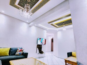 A modern interior with a chandelier, a flat-screen TV, and a sofa with colorful cushions.