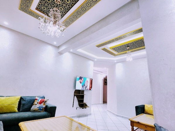 A modern interior with a chandelier, a flat-screen TV, and a sofa with colorful cushions.