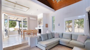 A spacious living area with a large grey sectional sofa, a dining table with chairs, and a staircase leading to an outdoor patio.