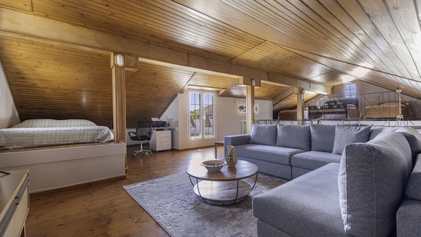 A spacious loft bedroom with a large bed, a grey sofa, and a wooden ceiling.