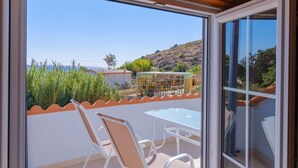 A balcony with a table and chairs, a view of the sea, and a hillside in the background.