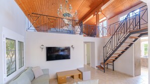 A spacious living area with a large flat-screen TV mounted on the wall, a wooden bench, and a staircase leading to an upper level.
