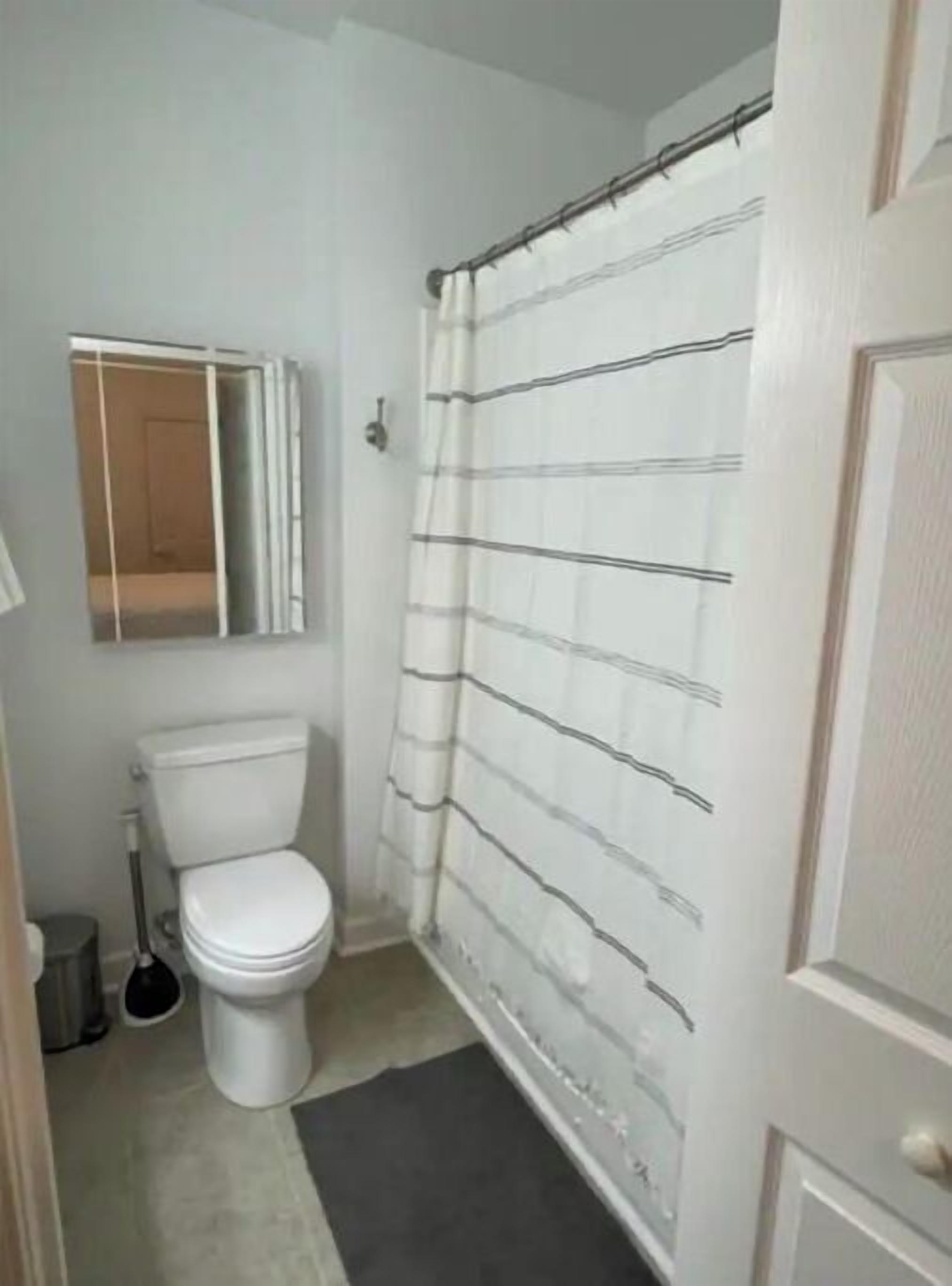 Un baño pequeño con inodoro, cortina de ducha y un espejo sobre el inodoro.