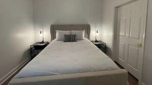 Une chambre d’hôtel étroite, avec un lit simple, deux tables de chevet et une porte.