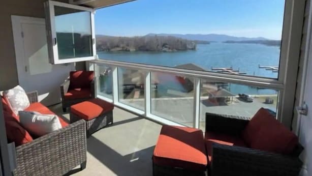 Un balcon doté de meubles en osier, d’un téléviseur et offrant une vue sur un lac et des montagnes.