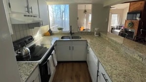 Uma cozinha compacta com armários brancos, bancada de granito e piso de madeira.
