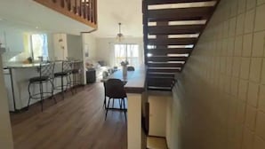 Uma sala de estar espaçosa com escada de madeira, cozinha com banquetas e área de jantar.
