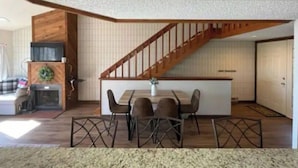 Cozinha moderna com escada de madeira, sala de jantar com mesa e cadeiras, e lareira.