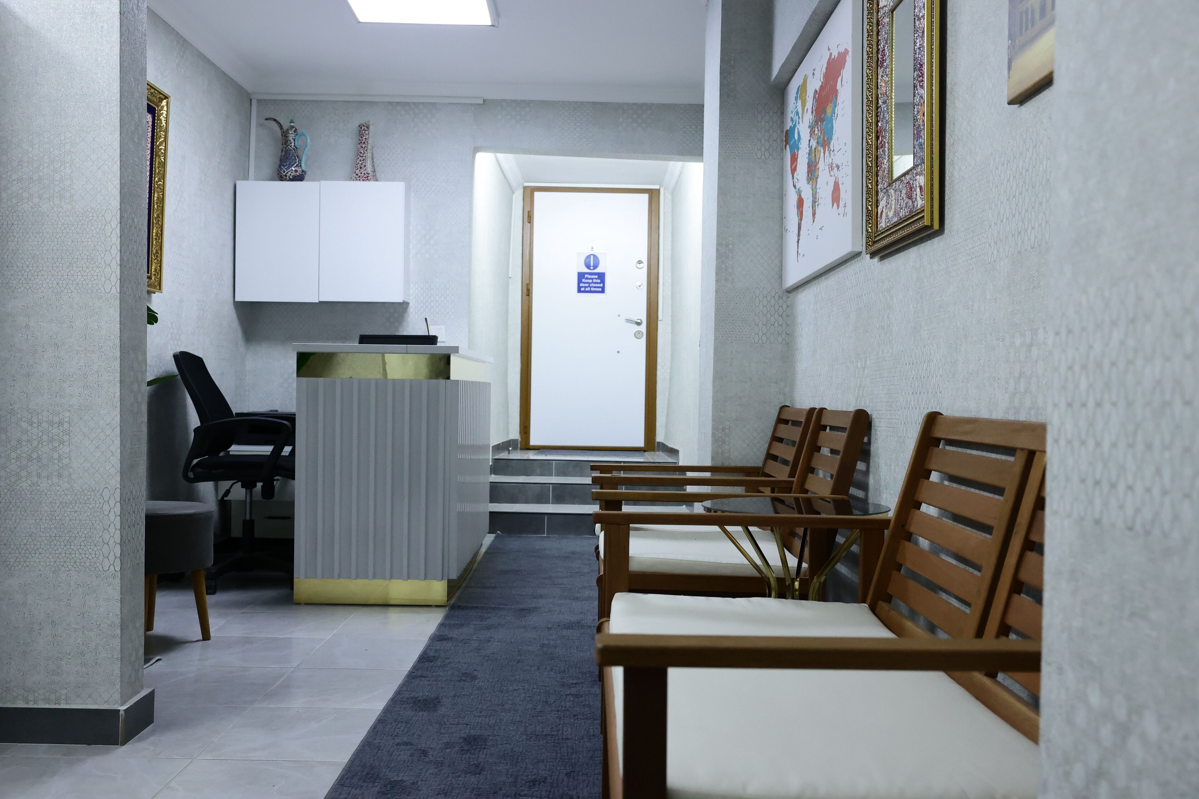 A hallway with a reception desk, a waiting area with wooden chairs, and a staircase leading to an upper floor.