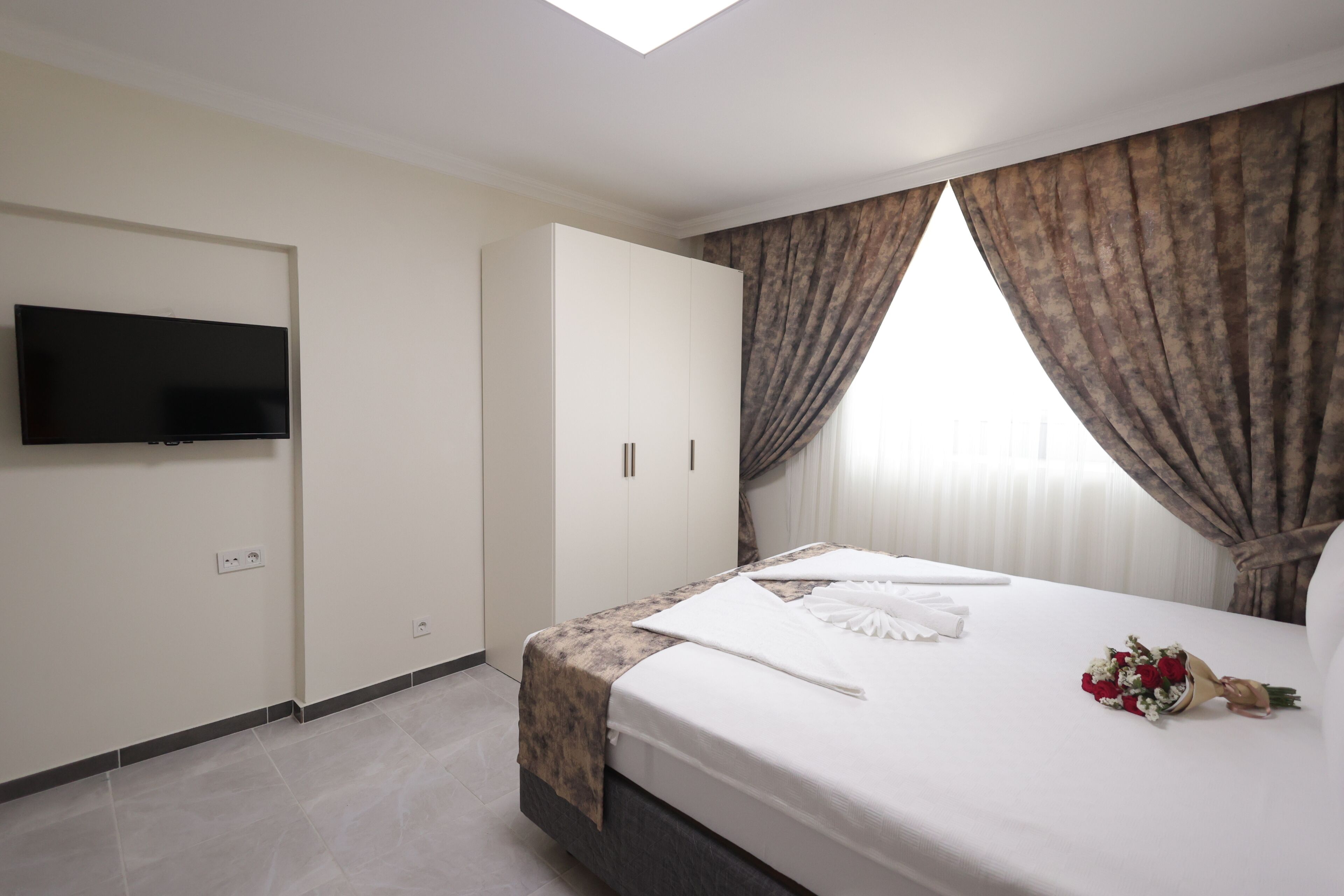Een hotelkamer met een bed, een flatscreen-tv, een kledingkast en een raam met gordijnen.