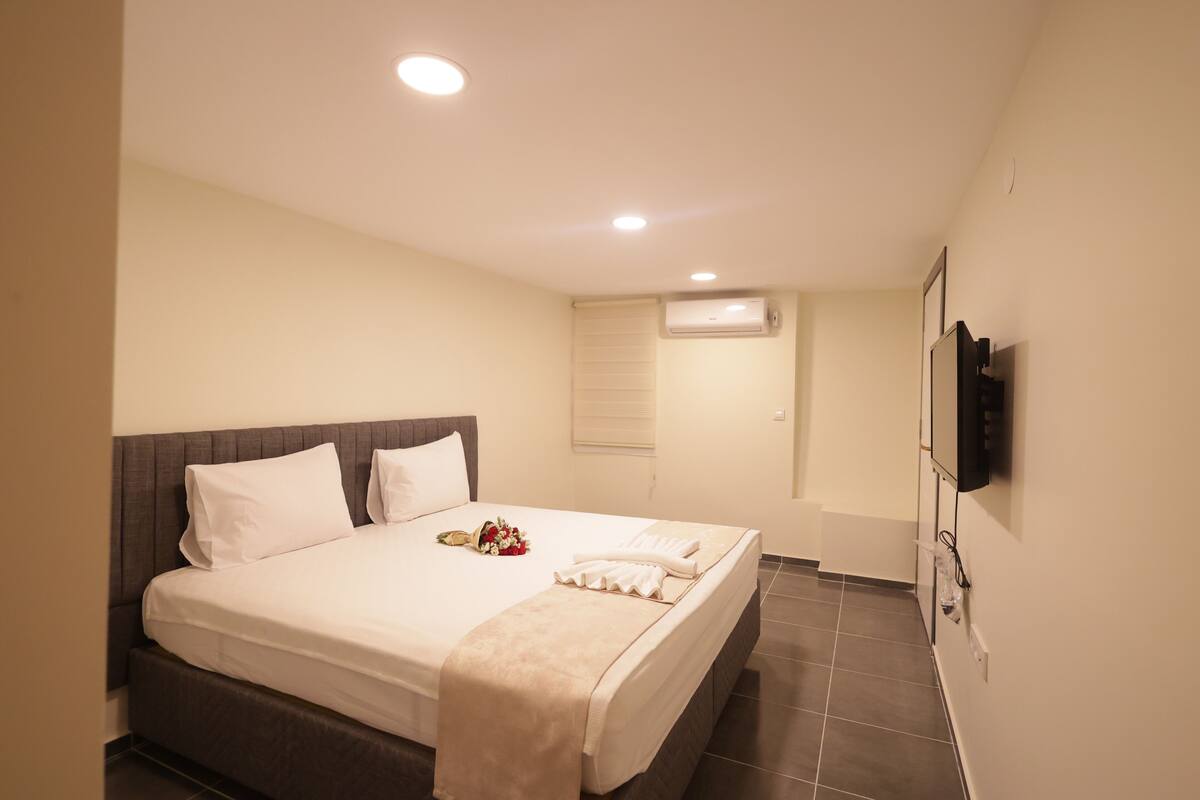 Una habitación de hotel con una cama grande, un televisor de pantalla plana montado en la pared y un equipo de aire acondicionado en la pared.