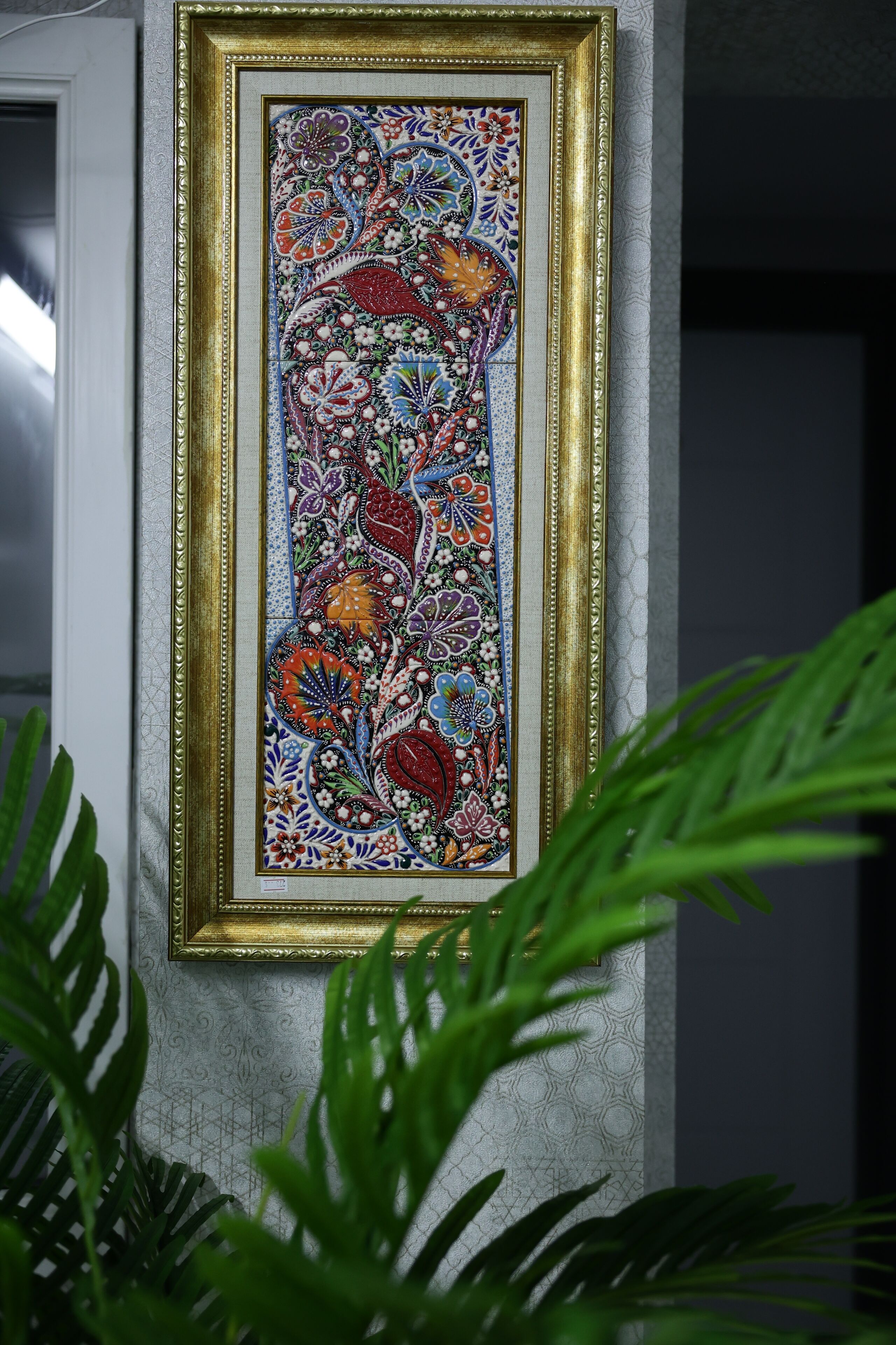 A framed artwork with intricate patterns and a gold frame, displayed on a textured wall.