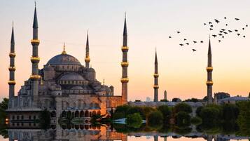 A historic mosque with multiple minarets and a large dome, surrounded by a calm body of water reflecting the structure.