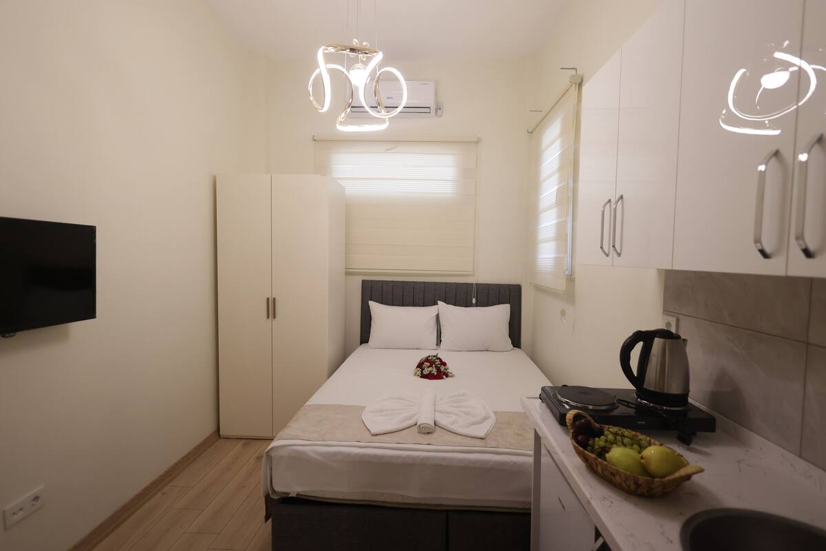 Habitación de hotel con cama, televisor de pantalla plana, armario, zona de cocina con tetera y frutero.