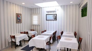 A dining area with striped wallpaper, white tables with placemats, and wooden chairs.