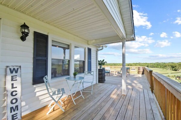 A wooden deck with a 'WELCOME' sign, a table with chairs, and a view of a golf course. - Mountain View Cottage @ 66-acre Horse Farm (Berryville)