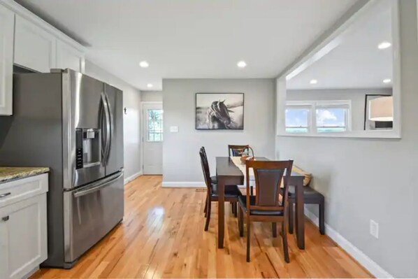 A modern kitchen with stainless steel appliances, a dining area with wooden chairs, and a gray wall with a framed picture. - Mountain View Cottage @ 66-acre Horse Farm (Berryville)