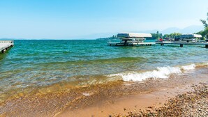 Ein Strand mit klarem Wasser, Kieselsteinen und einer Anlegestelle mit Booten.