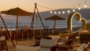 Un área de estar junto a la playa con sillas de mimbre y sombrillas de paja, con vista al océano.