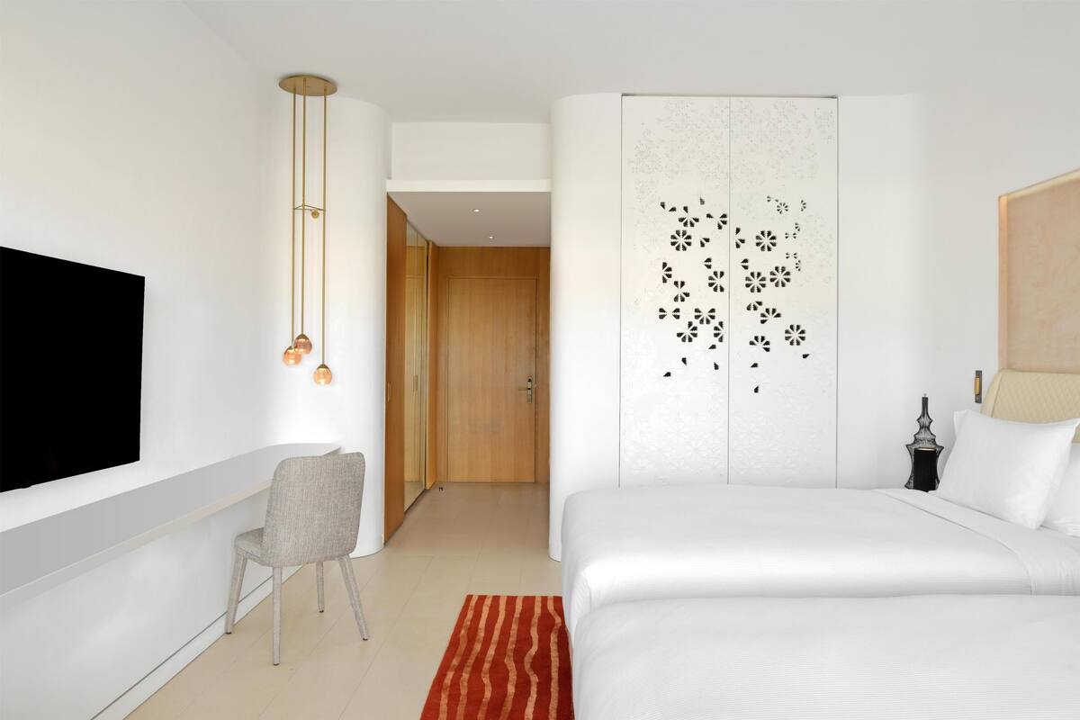 Een moderne hotelkamer met een bed, een televisie, een stoel en een decoratief wandpaneel.