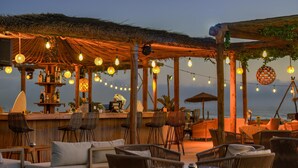 Un área de bar al aire libre con mobiliario de mimbre, techo de paja y luces colgantes.