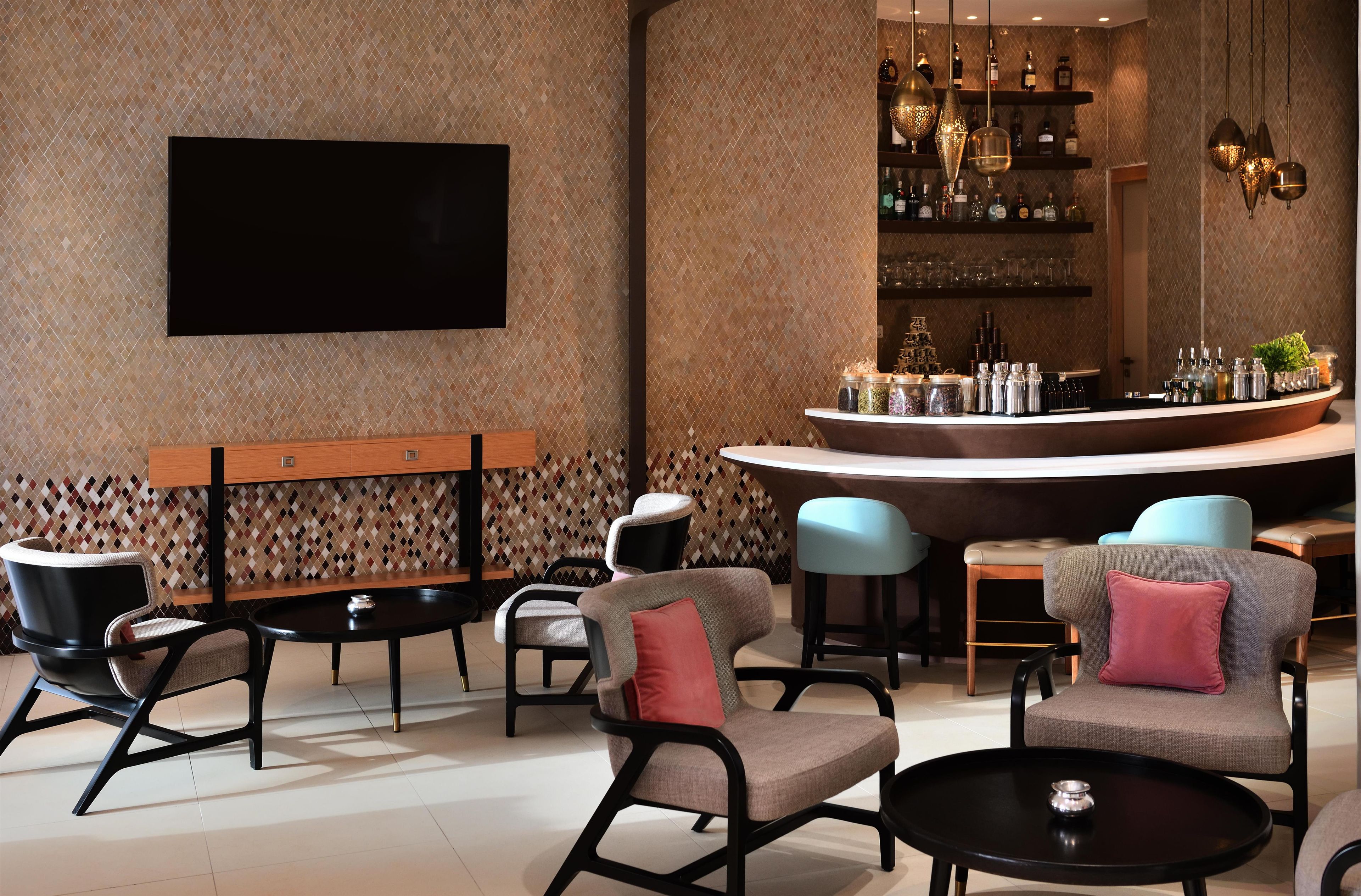 A modern bar area with seating, a flat-screen TV, and a variety of bottles and glasses on shelves.