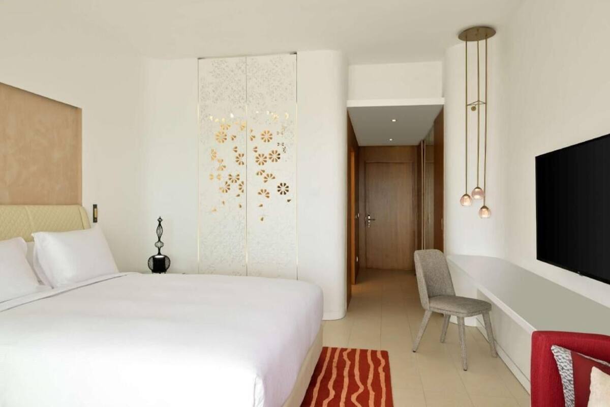 Een hotelkamer met een bed, een bureau, een stoel, een televisie en een decoratief wandpaneel.