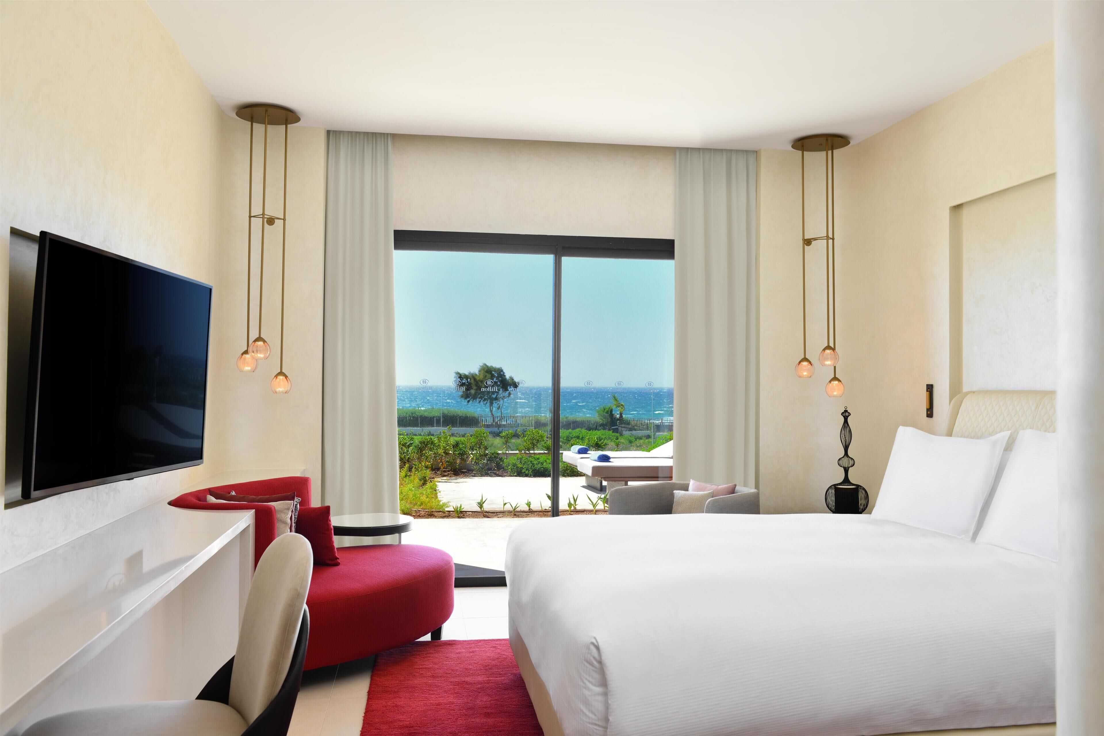 A hotel room with a bed, a TV, a desk, and a view of the outdoors.