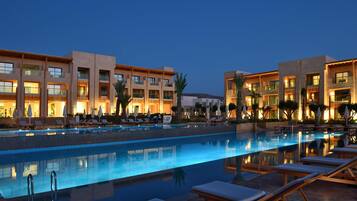 A hotel with a swimming pool, sun loungers, and a well-lit facade.