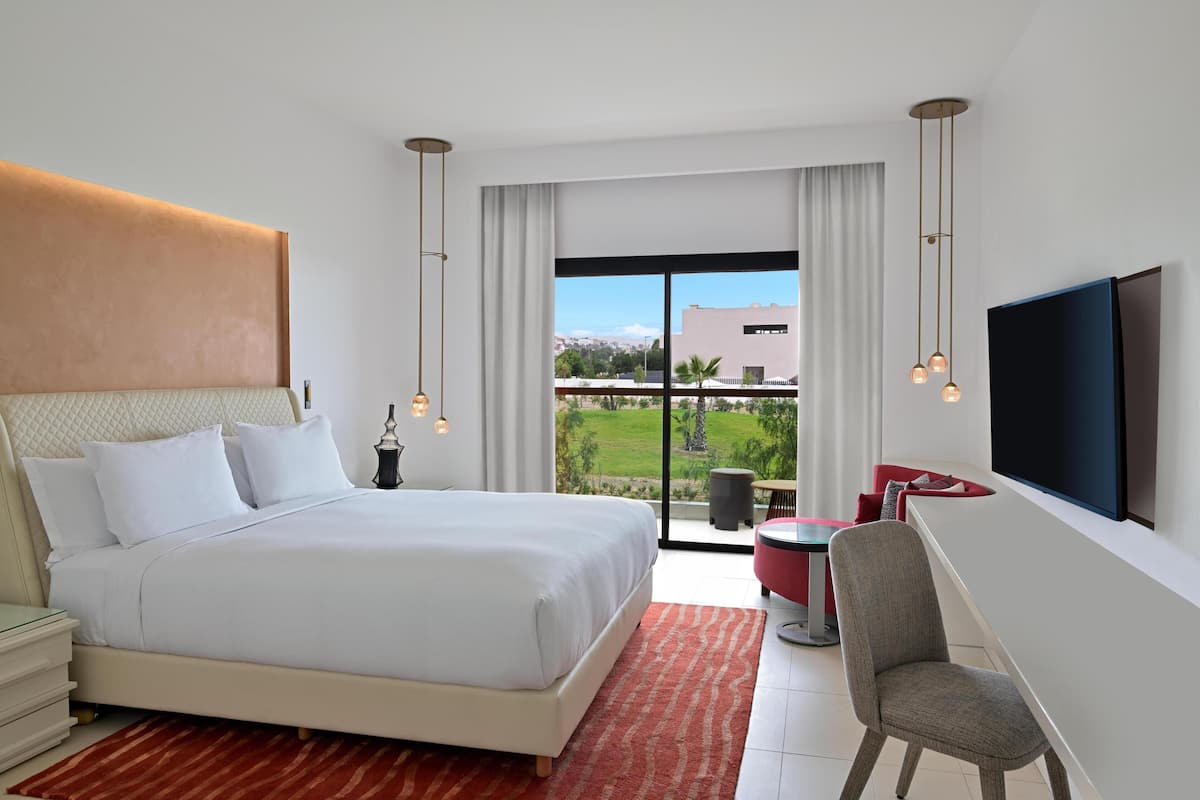 Een moderne hotelkamer met een groot bed, een televisie, een zithoek en uitzicht op het omliggende landschap.