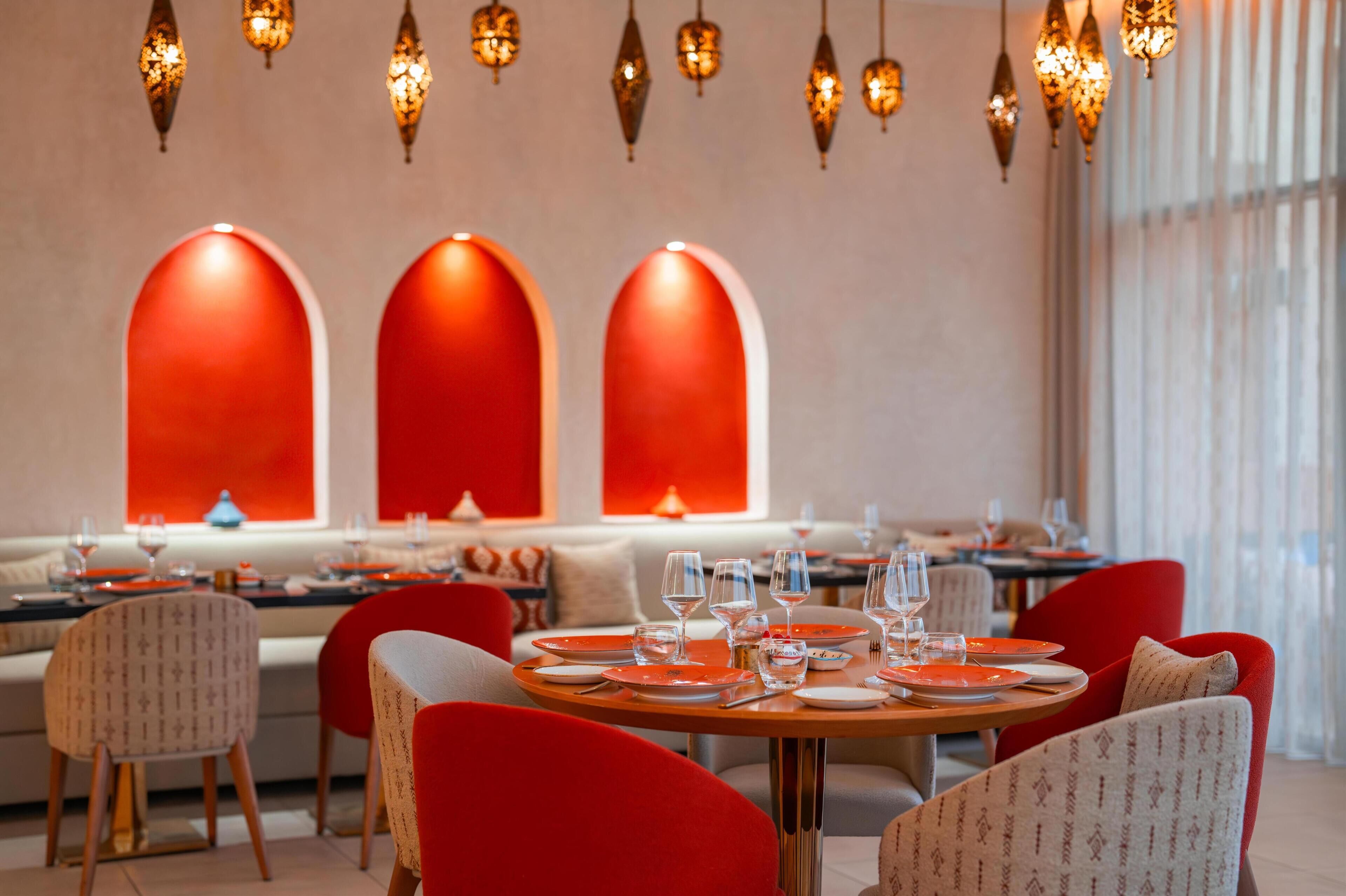 Ein Restaurant mit runden Tischen, roten Stühlen und hängenden Lampen.