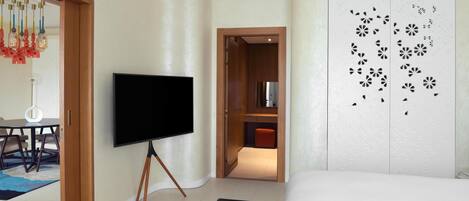 A hotel room with a bed, a TV on a stand, a dining area with a table and chairs, and a closet with patterned doors.