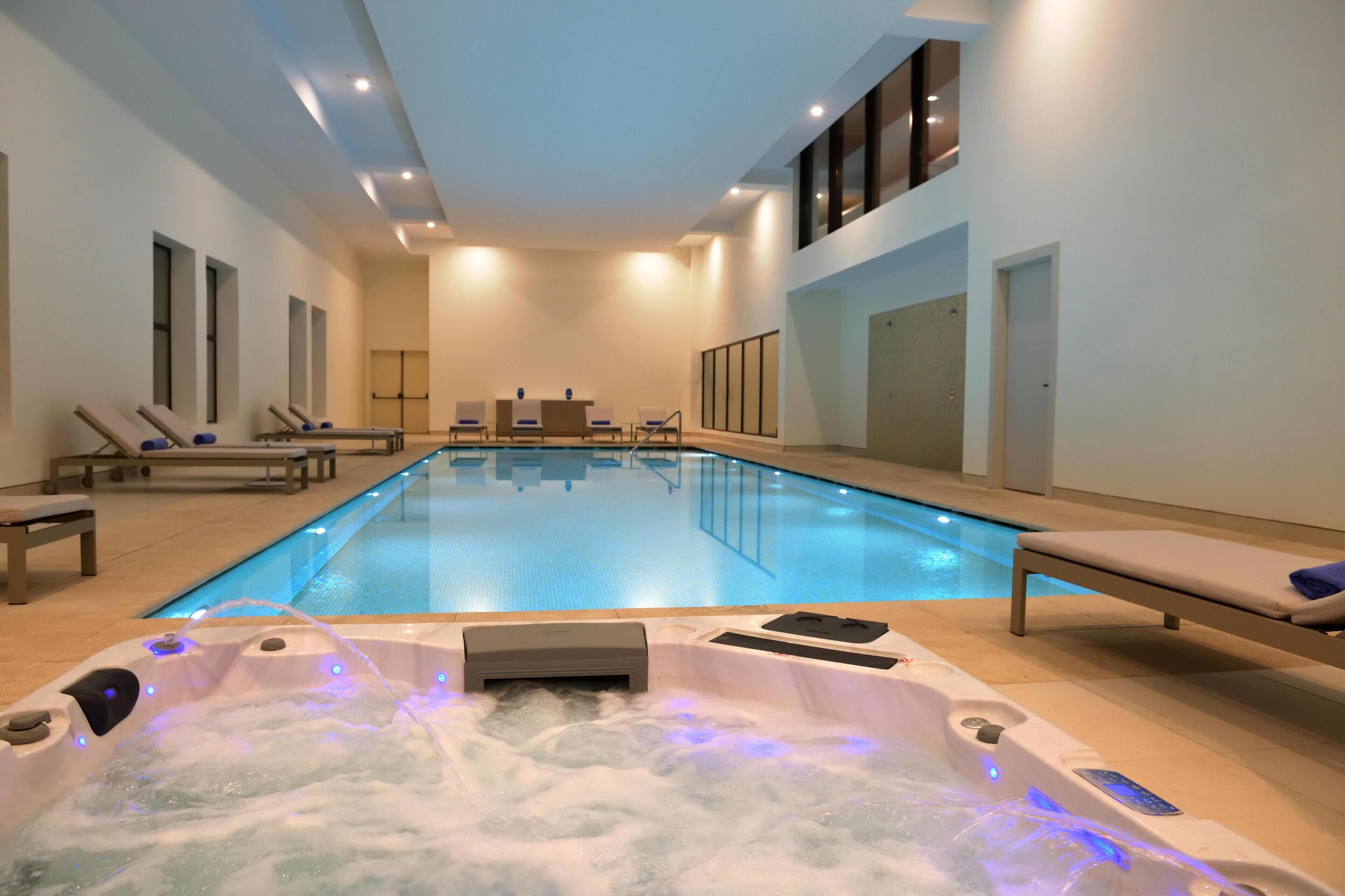 Une piscine avec des chaises longues et un espace équipé d’un jacuzzi.