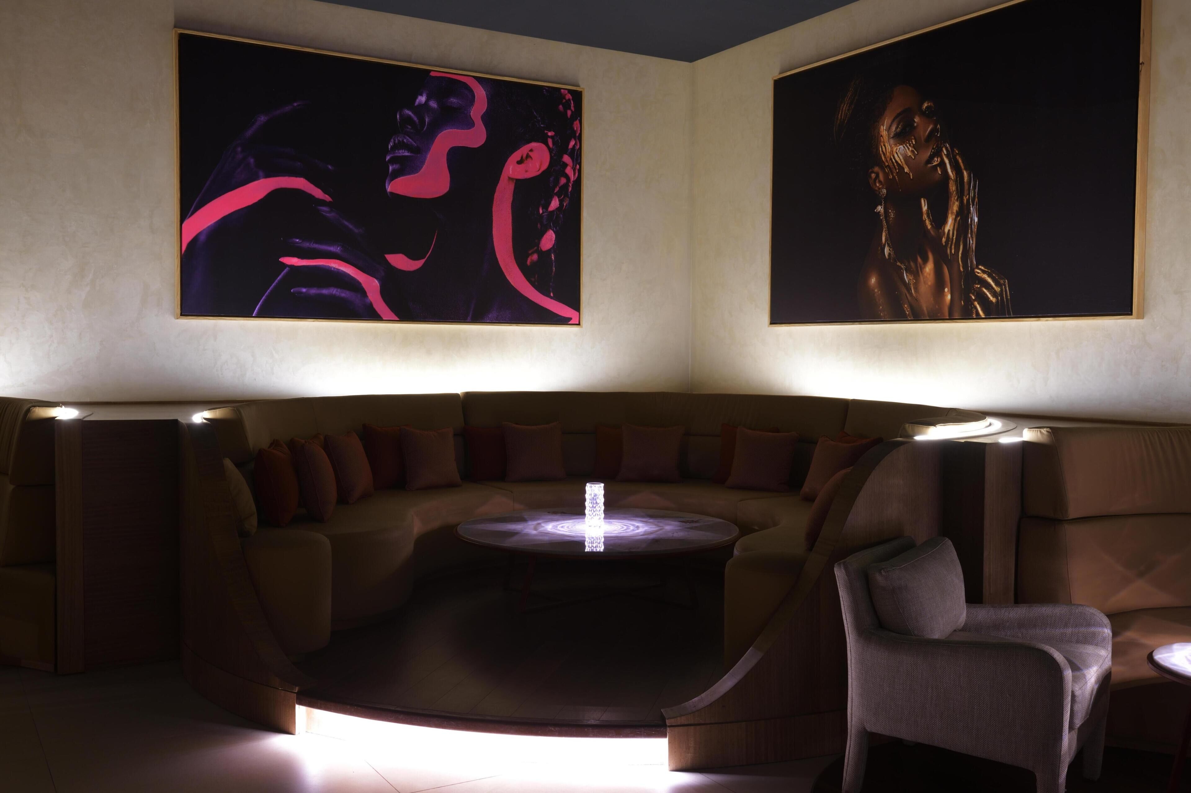A modern lounge with a curved sofa, a round table, and two large wall-mounted artworks.