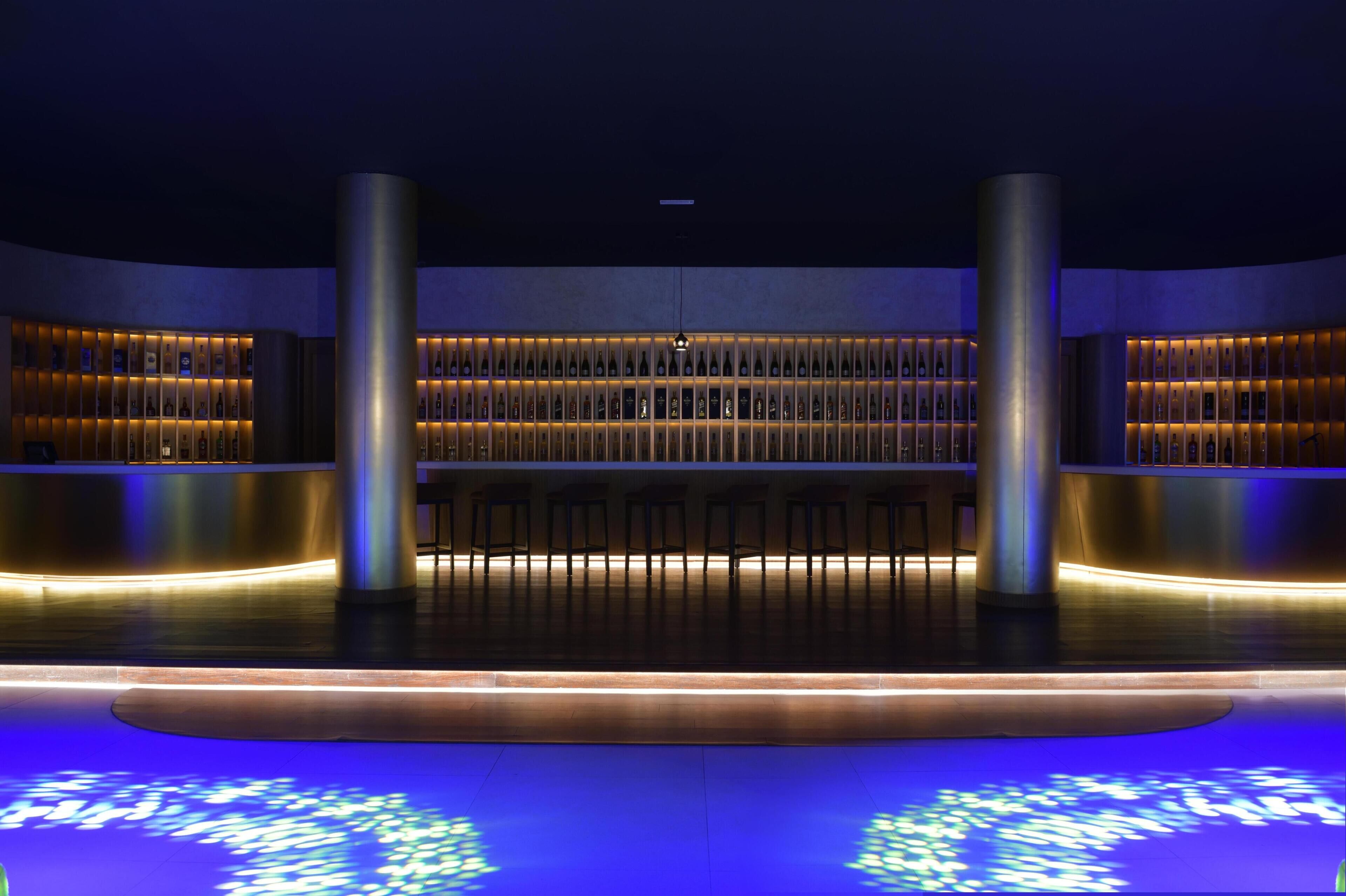 A modern interior with a central seating area, illuminated shelves, and a reflective floor.