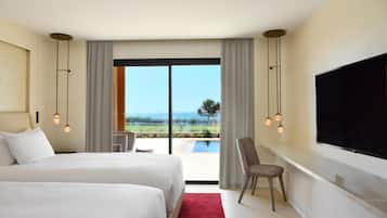 Habitación de hotel con dos camas, televisión, una silla, escritorio y un ventanal con vistas.
