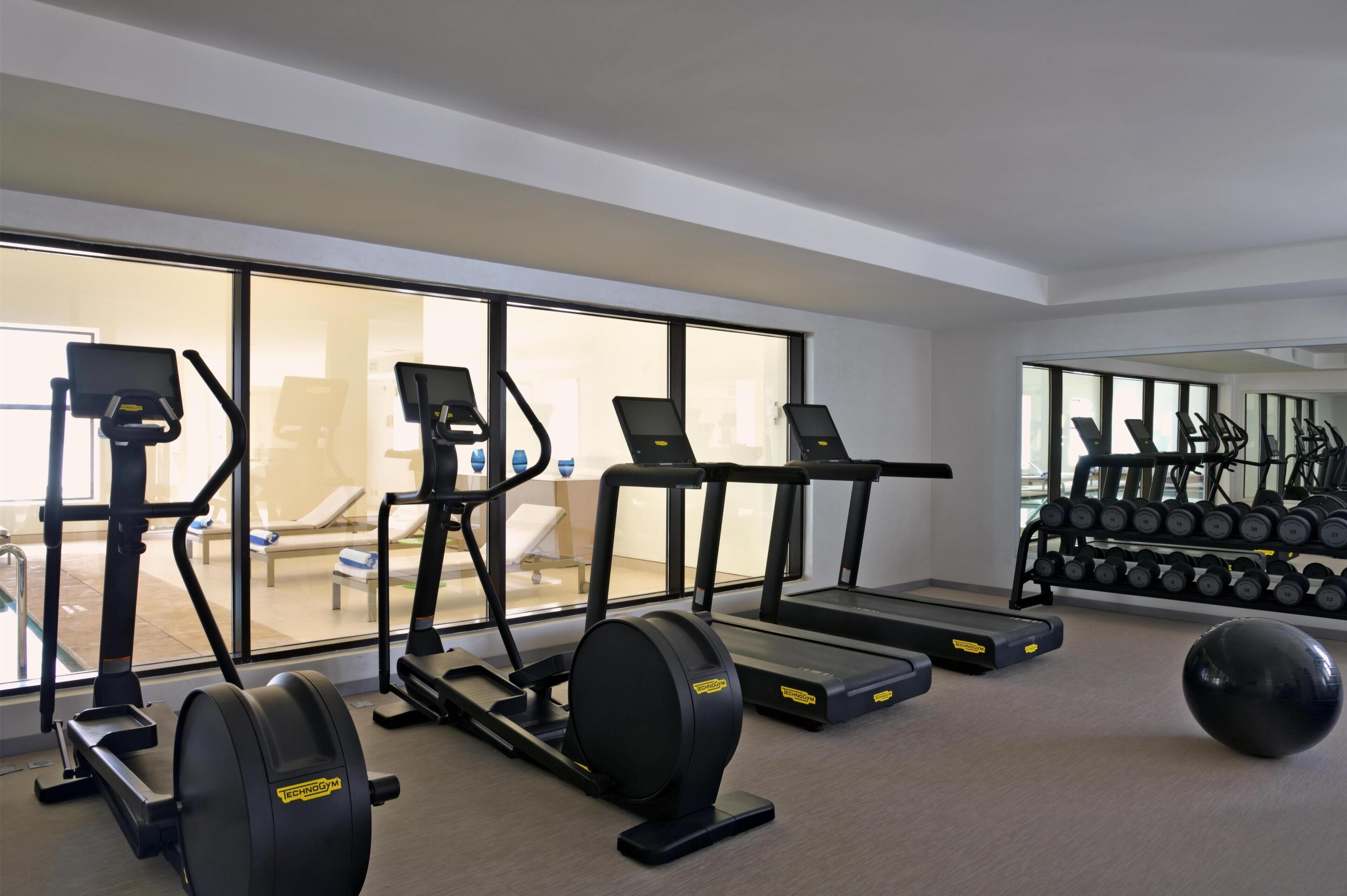 A gym with treadmills, an elliptical, a rowing machine, and a set of dumbbells.