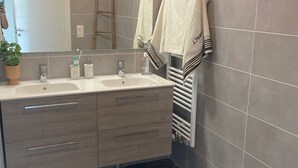 Une salle de bain moderne avec un meuble-lavabo à deux vasques, un porte-serviettes et une petite poubelle.