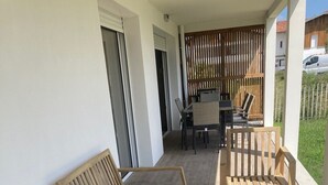 Une terrasse en bois avec deux chaises longues et une petite table, un tapis à motifs et une vue sur un quartier résidentiel.