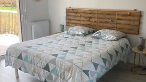 Une chambre à coucher avec une tête de lit en bois, une couvre-lit à motifs, un luminaire suspendu et une vue sur l’extérieur grâce à une porte coulissante.
